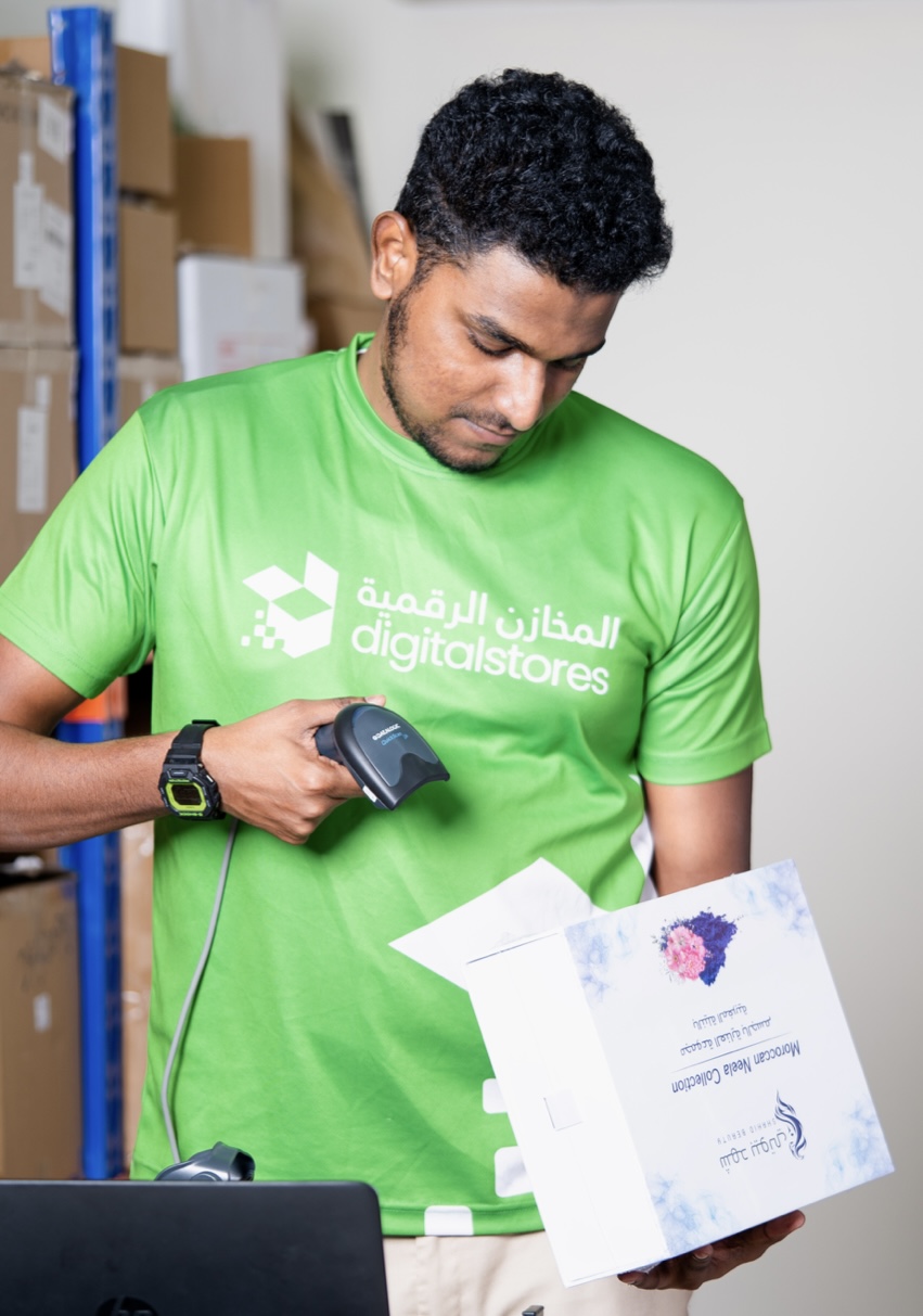 A DigitalStores associate in a branded green uniform scanning a customer package with a handheld barcode scanner